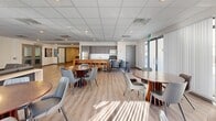 Located at 700 King St W in London, Ontario, this well-appointed amenity space offers a thoughtfully designed single-floor layout that serves as a versatile communal hub. Throughout the space, light wood-look flooring, a suspended tile ceiling with recessed and flush lighting, and large windows with vertical blinds create a bright, modern atmosphere.

The main lounge area is anchored by a sleek linear fireplace set within a full-height wood-panel feature wall, complemented by contemporary seating and open shelving displays. Large floor-to-ceiling windows flood this area with natural light. Adjacent to the lounge, a striking dark wood reception-style island serves as a central focal point, with open-plan dining beyond featuring multiple round tables and modern chairs.

The fully equipped kitchen includes stainless steel appliances, a gas range, built-in microwave, ample cabinetry, and a breakfast bar with seating — ideal for social gatherings. A dedicated games room provides space for a billiards table, foosball table, card table, and additional recreation, with teal accent walls adding a playful touch. The space also includes a closet for storage and is accessible via elevator, making it a fully functional and inviting amenity floor for building residents.