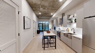 Located at 3030 Potomac Ave in Arlington, VA, this thoughtfully designed one-bedroom, one-bathroom residence blends industrial aesthetics with contemporary finishes throughout its efficiently organized floor plan. The open-concept kitchen and living area serves as the heart of the unit, where striking exposed concrete ceilings create dramatic visual contrast against crisp white walls and light wood flooring. The kitchen is outfitted with sleek gray flat-front cabinetry, stainless steel appliances including a gas range and bottom-freezer refrigerator, a deep undermount sink with a matte black faucet, and a white marble-top island with bar seating — ideal for both meal prep and casual dining. The living room enjoys abundant natural light through floor-to-ceiling glass doors that open directly onto a private balcony, offering outdoor views of the surrounding Arlington neighborhood. The bedroom is a serene retreat, also featuring balcony access via glass sliding doors, light-filled interiors, and ample space. The bathroom is finished with large-format gray tile flooring, a glass-enclosed walk-in shower with tile surround, and a clean-lined vanity. An adjacent walk-in closet with built-in shelving provides generous storage. Recessed lighting throughout adds a polished, modern touch to every room.