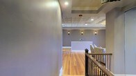 Located at 1301 Washington St in the heart of Vicksburg, Mississippi, this single-floor commercial space blends historic charm with refined, modern touches. The interior immediately draws attention with its standout ornate tin ceiling, a hallmark of classic Southern architecture that adds texture and visual interest overhead. Recessed lighting complements the decorative ceiling while wall-mounted sconces cast a warm, ambient glow throughout the space, creating an inviting and professional atmosphere. Rich hardwood floors in a natural finish run throughout, adding warmth and a sense of timeless elegance underfoot. A clean, white reception desk serves as a central focal point, positioned to welcome guests and anchor the main area. Comfortable seating with patterned upholstery adds a tasteful decorative touch. Crisp white crown molding and baseboards contrast beautifully against the soft gray walls, lending the space a polished, well-appointed feel. A staircase with dark wood railings and wrought iron balusters connects to adjacent levels, adding architectural depth. This space is well-suited for a boutique business, professional office, or hospitality use, offering a sophisticated environment that reflects Vicksburg's rich historical character.
