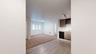 This 2-bedroom, 2-bathroom unit offers a practical and modern single-floor layout designed to maximize functionality. The open-concept living and kitchen area serves as the central hub of the space, where light wood-tone luxury vinyl plank flooring flows seamlessly from the kitchen into the living area, transitioning to warm beige carpet in the living zone. A window with vertical blinds brings in natural light, enhancing the bright, airy feel of the main area.

The kitchen is well-appointed with medium wood-toned cabinetry extending to the ceiling for ample storage, white countertops, and a full suite of black appliances including an electric range, over-the-range microwave, dishwasher, and refrigerator. A track lighting fixture overhead ensures the kitchen is well lit.

Both bedrooms are carpeted and offer a clean, neutral finish. The primary bedroom includes a closet with a sliding door and built-in rod. The two bathrooms each feature wood-toned vanities with white countertops, single-basin sinks, large mirrors, and light wood-look tile flooring, providing a cohesive and contemporary finish throughout the unit.
