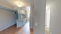 Located at 43444 16th St W in Lancaster, California, this single-story unit offers a practical and well-maintained layout designed for comfortable everyday living. The galley-style kitchen is a standout feature, equipped with stainless steel appliances including a gas range, over-the-range microwave, and refrigerator. Gray-toned cabinetry lines both sides of the kitchen, complemented by light countertops and a stainless steel sink. Light wood-style flooring runs through the kitchen and extends into the adjacent living and dining areas, creating a cohesive, open feel. The living area is carpeted and features a neutral color palette that keeps the space feeling bright and welcoming. Two bedrooms are each finished with plush carpet flooring, soft gray walls, and textured ceilings. Both rooms include mirrored sliding closet doors — one bedroom features an open shelving closet system visible behind the mirrored doors, offering organized storage solutions. Windows fitted with vertical blinds allow natural light to filter into the bedrooms. The bathroom is clean and straightforward, featuring a tub-shower combination, a speckled countertop vanity, and a medicine cabinet mirror. Overall, the space presents a tidy, move-in-ready environment with consistent finishes throughout.