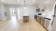 Located at 151 N Sixth St in Newark, NJ, this modern 2-bedroom, 1-bathroom unit offers a thoughtfully designed single-floor layout with contemporary finishes throughout. Light hardwood flooring flows seamlessly across the entire space, creating a bright and cohesive feel.

The open-concept kitchen serves as the heart of the unit, featuring light wood cabinetry, a white subway tile backsplash, a white quartz-topped center island with pendant lighting overhead, and a full suite of stainless steel appliances including a refrigerator, electric range, dishwasher, and microwave. Recessed lighting illuminates the space efficiently.

The two bedrooms are bright and airy, with large black-framed windows that invite natural light and offer views of mature trees. Both rooms continue the light hardwood flooring, and the primary bedroom includes a dedicated closet for ample storage.

The bathroom is finished with striking marble-look wall tile surrounding a full soaking tub and shower, complemented by light large-format floor tile, a wood-toned vanity with a white countertop, and a round mirror with modern wall lighting.

Overall, the unit presents a clean, modern aesthetic with neutral tones and quality finishes throughout, making it a well-appointed and functional living space.