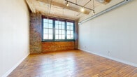 This single-floor loft unit masterfully blends industrial heritage with modern functionality. The main living area is defined by its striking exposed brick walls, original hardwood floors, and large multi-pane factory-style windows that frame open sky views and flood the space with abundant natural light. Overhead, an exposed ceiling with visible ductwork and track lighting reinforces the loft's authentic industrial character.

The kitchen is well-appointed with warm wood cabinetry extending to the ceiling, granite countertops, stainless steel appliances including a gas range, built-in microwave, and a French door refrigerator. A peninsula island with a granite surface provides additional prep space and defines the transition to the adjacent dining area.

The entry corridor benefits from high ceilings and features a transom window above the front door, allowing natural light to filter through. Hardwood floors continue seamlessly throughout, adding warmth and continuity to the space.

The bathroom is thoughtfully designed with a granite-topped vanity, warm wood cabinetry, a frameless glass-enclosed walk-in shower with tile surround, and the added convenience of a stacked in-unit washer and dryer. Together, these features make this loft a well-rounded, functionally complete space with strong architectural personality.