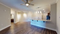 This single-story residence is designed around an open-concept layout that seamlessly connects the kitchen and living area, creating a spacious and functional living environment. Rich, dark hardwood-style flooring runs throughout the main living spaces, complemented by crown molding and ceiling fans that contribute to a polished, cohesive aesthetic.

The kitchen serves as a central focal point, featuring a large island with granite countertops and an integrated sink, providing both prep space and casual seating with bar-height overhang. Dark espresso cabinetry extends to the ceiling, offering generous storage, while a white subway tile backsplash adds a clean contrast. Stainless steel appliances, including a refrigerator, range, and over-the-range microwave, complete the kitchen. Pendant lighting above the island provides targeted task illumination.

The living area is generously proportioned with recessed lighting, a ceiling fan, and access to the exterior through French doors that allow natural light to filter in. Bedrooms feature plush carpeting, ceiling fans, and ample closet space, with the primary bedroom including a walk-in closet and an en-suite bath. The bathroom is finished with dark cabinetry, granite countertops, wood-style flooring, and a tub-shower combination.