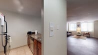 This single-floor residence offers a practical and comfortable layout across several well-defined living spaces. The kitchen is outfitted with rich cherry wood cabinetry, dark stone-finish countertops, and a full suite of appliances including a coil-burner range, over-the-range microwave, and dishwasher. A wet bar or utility counter area with a sink and additional cabinetry provides extra prep and storage space. The living area features warm, dark hardwood flooring and neutral walls that create a clean, inviting atmosphere. A window with blinds allows natural light to fill the room, complementing the understated, modern furnishings. A secondary sitting or flex area with the same hardwood flooring offers additional versatile living space. The primary bedroom is carpeted and generously sized, with a connecting hallway leading to additional rooms. A second bedroom, also carpeted, features a built-in desk nook and a window for natural light, making it well-suited as a guest room or home office. The bathroom is a standout feature, offering a wide double-sink vanity with white cabinetry, bright overhead lighting, a large mirror, and hardwood-style flooring, with convenient access to a walk-in closet or laundry area.