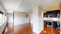 Located at 1919 Jackson St in the heart of Dallas, TX, this single-floor unit offers a well-designed layout with a clean, modern aesthetic throughout. Rich hardwood flooring extends across the main living areas, reflecting natural light and adding warmth to the neutral, light-toned walls.

The open living area is generously proportioned, with multiple windows framing urban cityscape views and allowing abundant natural light to fill the space. A ceiling fan adds both functionality and a finishing touch to the room.

The kitchen is outfitted with dark espresso cabinetry, stainless steel appliances including a smooth-top range and over-the-range microwave, and light solid-surface countertops — a practical and stylish space for cooking and entertaining.

The unit includes two bathrooms: one featuring a sleek glass-enclosed walk-in shower with white tile surround and a dark-cabinet vanity with backlit mirror, and a second with a clean white soaking tub and shower combination. Tile flooring runs through both bathrooms, providing a durable, easy-to-maintain surface.

The bedroom benefits from dual windows overlooking the Dallas skyline, a ceiling fan, and mirrored closet doors that enhance the sense of space. Overall, the unit presents a cohesive, contemporary living environment in a prime urban location.