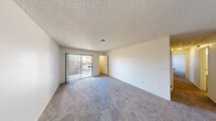 Located at 1307 Darlene Way in Boulder City, Nevada, this single-floor residence offers three bedrooms and two bathrooms within a practical and well-organized floor plan. The combined kitchen and living area serves as the central hub of the home. The kitchen is outfitted with white cabinetry, light countertops, black appliances including a range and refrigerator, a built-in dishwasher, and a stainless steel sink — all set over durable wood-look flooring. The living area features plush carpeting and a sliding glass door that invites natural light and provides outdoor access with views of surrounding greenery. Each of the three bedrooms is carpeted and finished with neutral walls and textured ceilings, creating a clean, understated aesthetic. The primary bedroom includes a sliding glass door, adding brightness and outdoor connectivity. Two closets provide practical storage throughout the unit. The two bathrooms are efficiently designed, each featuring a vanity with light countertops, a large mirror, and wood-look flooring. Overall, the space maintains a bright, functional character with consistent finishes and a straightforward layout suited for everyday living.
