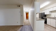 This single-floor unit offers a well-organized layout comprising two bedrooms, two bathrooms, a combined kitchen and living area, and a central hallway connecting all rooms. The living room serves as the focal point of the unit, featuring a brick-surround fireplace with a wood mantel and large sliding glass doors that open to a balcony, allowing natural light to fill the carpeted space. The entry door is positioned adjacent to the fireplace, with a vertical window providing additional light near the front entrance.

The galley-style kitchen is efficiently designed with white cabinetry lining both walls, granite-toned countertops, wood-look flooring, and black appliances including a refrigerator, range, and microwave. A double sink is positioned along one side, maximizing counter and storage space throughout.

The primary bedroom offers a comfortable footprint with carpet flooring, a sliding mirrored closet, and a window with vertical blinds. The second bedroom is similarly carpeted. Both bathrooms feature matching finishes, including white cabinetry, granite-toned countertops, large vanity mirrors, and wood-look flooring. The hallway, also carpeted, connects the bedrooms and bathrooms with a textured ceiling consistent throughout the unit.