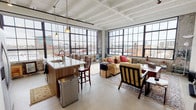 This one-bedroom, one-bathroom loft-style unit at Checker showcases an impressive industrial aesthetic rooted in the building's heritage. The open-plan living and kitchen area is defined by soaring coffered ceilings with white-painted beams and vast banks of black steel-frame windows that wrap the perimeter, flooding the space with natural light and offering panoramic city skyline views. Polished concrete floors run throughout, reinforcing the loft's industrial character.

The kitchen is thoughtfully appointed with warm wood cabinetry, a generous granite-topped island with seating, stainless steel appliances including a side-by-side refrigerator and electric range, and an over-the-range microwave. Exposed brick accents frame the kitchen's window wall, adding raw texture.

The living area benefits from the same dramatic window wall, framing sweeping urban views and creating an airy, light-filled atmosphere. The spacious bedroom continues the loft's aesthetic with exposed brick, steel-frame windows, a ceiling fan, and direct sightlines to the city beyond.

The bathroom is well-appointed with a long wood vanity, granite countertop, a glass-enclosed shower with subway tile, and open shelving for storage. The unit's blend of industrial architecture and modern finishes creates a distinctive, urban living experience.