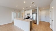 Located at 5948 Aretha Place in Virginia Beach, VA, this well-appointed single-floor home offers three bedrooms and two bathrooms within a thoughtfully designed layout. The open-concept living and kitchen area serves as the heart of the home, featuring light hardwood-style flooring that flows seamlessly throughout. The kitchen is a standout, centered around a large white island with an integrated sink, complemented by white shaker cabinetry, a subway tile backsplash, and a full suite of stainless steel appliances including a refrigerator, range, microwave, and dishwasher. Recessed lighting adds a clean, modern touch overhead. The spacious living room is bathed in natural light through multiple large windows fitted with horizontal blinds, and a ceiling fan provides year-round comfort. Sliding glass doors open to a private balcony with outdoor views. The bedrooms are carpeted for warmth and comfort, each with ample closet space — including a generously sized walk-in closet with wire shelving in the primary suite. The primary bathroom features a dual-sink vanity with navy blue cabinetry, white countertops, and a large mirror. The additional bedrooms include double-door closets. Clean neutral tones and contemporary finishes throughout give this home a bright, move-in-ready feel.