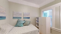 Located at 1010 10th St in Sacramento, CA, this compact studio unit is thoughtfully designed to maximize every square foot of its single-room footprint. The space is organized into distinct functional zones, making efficient use of its cozy layout. Warm-toned hardwood flooring runs throughout, lending a clean and cohesive feel to the interior. The sleeping area accommodates a twin bed with under-bed storage, complemented by a freestanding white wardrobe unit with open shelving — providing practical storage without overwhelming the space. Coastal-themed wall art adds a light, calming aesthetic to the soft sage-green walls. The kitchenette area is well-appointed with light gray shaker-style cabinetry, open shelving, a stainless steel sink with countertop space, a full-size stainless steel refrigerator, and a microwave — offering essential cooking amenities in a compact footprint. A full-length mirror and a sleek black accent chair round out the furnishings. Natural light enters through multiple windows fitted with blinds, brightening the space considerably. Crown molding details add a subtle architectural character. A wall-mounted climate control unit ensures year-round comfort. This efficiently designed space is well-suited for a single occupant prioritizing location and functionality in the heart of Sacramento.