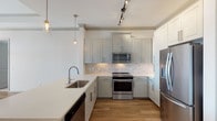 Located at 1719 W Campbell Rd in Garland, TX, this single-story residence presents a clean, modern aesthetic throughout its well-appointed interior. The kitchen serves as a central highlight, showcasing sage-toned shaker-style cabinetry paired with a classic marble-look tile backsplash. Stainless steel appliances — including a French door refrigerator, electric range, and built-in microwave — complement the crisp white quartz countertops and peninsula with an undermount sink. Warm-toned hardwood-style flooring runs through the main living and kitchen areas, while track lighting and glass pendant lights provide layered illumination.

The bedrooms feature neutral carpet flooring and bright white walls, creating a calm and versatile environment. The primary bedroom includes direct access to an en-suite bathroom finished with marble-look tile flooring, a vanity with granite countertops, and a walk-in shower with glass enclosure. A secondary bathroom offers a tub-shower combination with white tile surround, a granite-topped vanity, and a dark wood-framed mirror. Crown molding details and consistent neutral finishes throughout the space contribute to a cohesive, well-maintained overall ambiance.