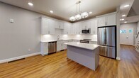 This three-floor home in Woburn, Massachusetts is thoughtfully designed with modern finishes throughout. The main living level features warm hardwood flooring, recessed lighting, and large windows that invite generous natural light. A glass-paneled exterior door provides direct outdoor access, enhancing the sense of openness. The kitchen is a standout, outfitted with white shaker cabinetry, quartz countertops, a central island with pendant lighting, and a full suite of stainless steel appliances including a refrigerator, range, microwave, and dishwasher.

Upper-level bedrooms are carpeted and well-proportioned, with large windows offering neighborhood views. One bedroom includes a walk-in closet with wire shelving systems for organized storage. Bathrooms feature light tile flooring, white vanities with quartz countertops, and brushed hardware accents. A lower-level bedroom includes its own closet and access to a private bathroom.

A staircase with a classic white balustrade connects all three floors. The unfinished basement level presents an open, flexible space with visible mechanicals, concrete flooring, and framed walls ready for future customization.