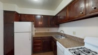Located at 1414-1422 SOM Center Rd in Mayfield Heights, Ohio, this single-floor residence offers a well-organized layout designed for comfortable everyday living. The kitchen is a functional highlight, outfitted with rich dark wood cabinetry, granite-style countertops, a stainless steel sink, and white appliances including a refrigerator, gas range, and dishwasher, all set over durable wood-style flooring. The living areas are generously sized, featuring neutral carpet throughout and large vertical blind-covered windows that allow ample natural light to fill the space. A ceiling fan adds comfort to the main living area, which connects smoothly to adjacent rooms via a clear, open hallway. The bedrooms are well-proportioned with plush carpet and clean white walls; the primary bedroom notably includes two separate closets, providing excellent storage capacity. The bathroom features wood-style flooring, white tile surround surrounding the bathtub, and a vanity with granite-style countertops that coordinate with the kitchen finishes. Throughout the residence, the design maintains a clean, neutral palette that offers a versatile backdrop for personalization. The overall layout, as seen in the floor plan, is efficiently arranged to maximize usable space across all rooms.