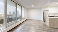 Located at 25 St Dennis Drive in Toronto's Don Mills neighbourhood, this 2-bedroom, 1-bathroom unit offers a thoughtfully designed single-floor layout with a clean, modern aesthetic throughout. Light wood-tone flooring runs continuously across all living areas, complementing the crisp white walls and creating a warm, cohesive atmosphere.

The open-concept living and dining area is generously proportioned, bathed in natural light through expansive floor-to-ceiling sliding glass windows that frame impressive city skyline views and provide access to a balcony. Recessed lighting adds a polished touch overhead.

The kitchen is efficiently designed with two-tone cabinetry — white upper cabinets paired with natural wood lower cabinets — topped with light stone countertops. Stainless steel appliances, including a refrigerator and dishwasher, complete the functional space.

Both bedrooms are well-sized, each featuring large windows with city views, light hardwood flooring, and double-door closets offering ample storage. The primary bedroom is particularly spacious. The bathroom is finished with tile flooring, a combined tub and shower, and a vanity with wood cabinetry. Four closets throughout the unit provide excellent storage capacity.