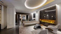 Located in the heart of Chicago's Lincoln Park neighborhood, this single-floor amenity space at 310 W Belden Ave delivers a refined, hotel-inspired atmosphere through meticulous design and high-end finishes. The main lounge area is anchored by a dramatic oval tray ceiling with integrated ambient lighting that casts a warm glow across the room. A full-height dark marble fireplace wall with a linear ethanol flame serves as a striking focal point, complemented by plush seating arrangements that invite relaxed conversation. Steel-framed glass partitions allow natural light to filter through while maintaining distinct zones within the space. An adjacent dining area features a statement crystal chandelier suspended above a sleek marble-backed dining table, offering an elevated setting for private gatherings. Transitioning into the entertainment zone, a billiards room exudes a moodier, club-like ambiance with dark wainscoting, herringbone-patterned slate flooring, pendant lighting, and a wet bar with barstool seating. Throughout, the design palette balances warm neutrals, deep charcoals, and polished marble surfaces, creating a cohesive and sophisticated environment ideal for both social and intimate occasions.