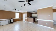 This single-floor home offers an open-concept design that seamlessly connects the living area and kitchen, creating a spacious and functional layout. The interior is finished with light-toned ceramic tile flooring throughout, providing a clean and cohesive look underfoot. Warm earth-toned walls, accented by crisp white crown molding and baseboards, add a classic character to the space.

The living area is generously sized, benefiting from a large window that invites natural light and two ceiling fans that ensure comfortable airflow across the open floor plan. The kitchen features a peninsula-style counter with a raised breakfast bar, dark countertops, and a tile backsplash that adds a decorative touch. White cabinetry provides ample storage, and the layout allows for easy interaction between the kitchen and the living space.

Recessed lighting in the ceiling complements the natural light, ensuring the space remains bright throughout the day. The combination of practical finishes, an open floor plan, and thoughtful design details makes this a well-appointed and comfortable single-story home suited for everyday living.