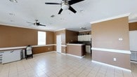 This single-floor home offers an open-concept design that seamlessly connects the living area and kitchen, creating a spacious and functional layout. The interior is finished with light-toned ceramic tile flooring throughout, providing a clean and cohesive look underfoot. Warm earth-toned walls, accented by crisp white crown molding and baseboards, add a classic character to the space.

The living area is generously sized, benefiting from a large window that invites natural light and two ceiling fans that ensure comfortable airflow across the open floor plan. The kitchen features a peninsula-style counter with a raised breakfast bar, dark countertops, and a tile backsplash that adds a decorative touch. White cabinetry provides ample storage, and the layout allows for easy interaction between the kitchen and the living space.

Recessed lighting in the ceiling complements the natural light, ensuring the space remains bright throughout the day. The combination of practical finishes, an open floor plan, and thoughtful design details makes this a well-appointed and comfortable single-story home suited for everyday living.