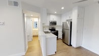 Located at 5825 Reseda Blvd in the Tarzana neighborhood of Los Angeles, this single-floor unit offers a clean, modern aesthetic throughout. The kitchen is a standout feature, designed with crisp white shaker cabinetry, light quartz countertops, and a peninsula with an integrated sink — ideal for both meal prep and casual dining. Stainless steel appliances, including a refrigerator, electric range, and over-the-range microwave, complete the well-equipped culinary space. Light wood-look flooring runs through the kitchen and main living areas, contributing to a bright and cohesive feel. The open layout connects the kitchen to the living area, which benefits from recessed lighting and a ceiling fan, along with a sliding glass door that allows natural light to filter in. The bedrooms are finished with plush neutral carpeting and recessed lighting, offering a comfortable retreat. One bedroom includes a closet with mirrored doors. Additional rooms feature vertical blinds on the windows for light control and privacy. The overall color palette — soft whites and warm neutrals — gives the space a fresh, move-in-ready appearance throughout.