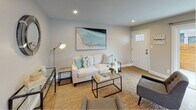 This single-floor residence showcases a thoughtfully designed interior with a cohesive, modern aesthetic carried throughout each room. The kitchen is a standout feature, outfitted with rich dark cabinetry, crisp white quartz countertops, and a herringbone-patterned tile backsplash. Stainless steel appliances — including a gas range, built-in microwave, dishwasher, and refrigerator — provide a fully equipped cooking space. A pendant light fixture hangs above the sink area, which is illuminated by a window overlooking the exterior, adding natural light to the space.

The living area is bright and welcoming, with recessed lighting, neutral grey walls, and warm hardwood-style flooring that extends seamlessly throughout the home. A front entry door with a transom window brings in additional natural light, enhancing the airy feel of the space.

The two bedrooms are comfortably sized, each with windows providing natural light. One bedroom features mirrored sliding closet doors, adding a sense of depth to the room.

The bathroom is clean and contemporary, featuring large-format floor tiles, a floating dark vanity with a white basin, and a soaker tub enclosed by a sliding glass panel, with a frosted window above providing privacy and light.