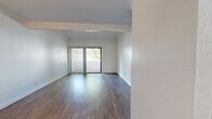 Located on Lindley Avenue in the Porter Ranch neighborhood of Los Angeles, this single-story, one-bedroom, two-bathroom unit offers a well-organized and functional layout. The combined kitchen and living area forms the heart of the space, featuring warm wood-style flooring that extends throughout the main living areas. The kitchen is designed with a peninsula-style pass-through counter, white cabinetry, grey countertops, a stainless steel sink, and built-in appliances including a microwave and range. Crown molding adds an architectural detail to the living room, which is filled with natural light through a full-width sliding glass door that opens to a private balcony overlooking mature, leafy trees. The bedroom is carpeted for comfort and features a window framing views of the surrounding greenery, creating a calm and restful atmosphere. Two full bathrooms serve the unit; one features a large vanity with white cabinetry, grey countertop, brushed nickel fixtures, and a mirror, alongside a separate tub and shower area finished in clean white. The overall aesthetic is bright and neutral throughout, with white walls providing a clean, move-in ready canvas. A ceiling fan is present in the living/dining area, adding to the practical comfort of the space.