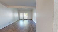 Located on Lindley Avenue in the Porter Ranch neighborhood of Los Angeles, this single-story, one-bedroom, two-bathroom unit offers a well-organized and functional layout. The combined kitchen and living area forms the heart of the space, featuring warm wood-style flooring that extends throughout the main living areas. The kitchen is designed with a peninsula-style pass-through counter, white cabinetry, grey countertops, a stainless steel sink, and built-in appliances including a microwave and range. Crown molding adds an architectural detail to the living room, which is filled with natural light through a full-width sliding glass door that opens to a private balcony overlooking mature, leafy trees. The bedroom is carpeted for comfort and features a window framing views of the surrounding greenery, creating a calm and restful atmosphere. Two full bathrooms serve the unit; one features a large vanity with white cabinetry, grey countertop, brushed nickel fixtures, and a mirror, alongside a separate tub and shower area finished in clean white. The overall aesthetic is bright and neutral throughout, with white walls providing a clean, move-in ready canvas. A ceiling fan is present in the living/dining area, adding to the practical comfort of the space.