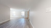 This single-floor space has been thoughtfully updated with a clean, modern aesthetic and a cohesive neutral color palette. The main living area is open and airy, featuring light gray wood-look flooring that extends throughout the common spaces, crisp white walls, and generous natural light provided by multiple windows fitted with blinds. A charming French door with glass pane detailing connects the living area to an adjacent room, adding an elegant architectural touch.

The kitchen is well-appointed with white shaker-style cabinetry, brushed gold hardware, and striking stone-look countertops. Stainless and black stainless appliances, including a range and over-the-range microwave, complete the functional and stylish cooking space.

The bedrooms are carpeted in a warm taupe tone, offering a comfortable contrast to the hard flooring elsewhere. One bedroom features dual sliding-door closets and a window overlooking the exterior, providing ample storage and natural light.

The bathroom is neatly finished with light wood-look tile flooring, a white shaker vanity with a mirrored medicine cabinet, and a tub-shower combination accented by warm travertine-style tile surround. Overall, the space presents a move-in-ready environment with consistent, updated finishes and a welcoming, bright ambiance throughout.