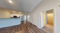 This single-story residence is thoughtfully designed with a neutral color palette and a clean, modern aesthetic throughout. The open-concept living area immediately impresses with soaring vaulted ceilings and dark hardwood-style flooring that extends seamlessly through the main living spaces. A ceiling fan with lighting anchors the living room, which benefits from natural light through French doors that lead to an outdoor area.

The kitchen is well-appointed with white shaker-style cabinetry, granite countertops, a deep undermount sink, and a full suite of stainless steel appliances including a refrigerator, range, microwave, and dishwasher. A breakfast bar provides additional prep and dining space, and the kitchen opens directly to the main living area for easy interaction.

Multiple bedrooms are carpeted for comfort and feature ceiling fans, window blinds for light control, and generous closet space, including at least one closet with built-in shelving and hanging rods. The bathroom includes a white vanity with a clean countertop, a framed mirror, and stone-tile flooring. A hallway lined with multiple doors provides access to additional storage and private spaces, contributing to the overall functional layout of the home.