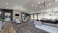 This sophisticated single-floor clubhouse and leasing center is designed with a contemporary aesthetic that balances professionalism and comfort. Upon entry, visitors are greeted by a grand arched doorway and soaring accent walls clad in white marble, setting an elegant tone for the space. A sleek, marble-faced reception desk anchors the front area, flanked by workstations equipped for staff, all beneath a striking sputnik-style chandelier.

The open layout flows seamlessly into a generously sized lounge area, where plush white wingback chairs and glass-topped coffee tables are arranged around a floor-to-ceiling stone accent wall. A linear electric fireplace is set into this wall beneath a wall-mounted flat-screen television, creating a warm and inviting focal point. Decorative artwork and sculptural wall accents in muted blues and grays complement the cool-toned color palette throughout.

Natural light pours into the space through expansive windows dressed with floor-length linen drapes, offering direct views of the outdoor pool area and surrounding grounds. A dedicated dining and meeting zone features bistro-style tables and chairs, ideal for casual gatherings. The floors transition between richly patterned carpet and wood-look tile, adding visual texture and defining the various zones within the space.