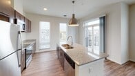 This single-floor residence offers a well-designed, open-concept layout where the kitchen flows seamlessly into the living area, creating a bright and cohesive living space. The kitchen is a standout feature, equipped with rich dark-wood cabinetry, granite countertops, and a full suite of stainless steel appliances including a range, built-in microwave, refrigerator, and dishwasher. A central island with an undermount sink and a stylish pendant light above serves as both a functional workspace and a natural gathering point. Multiple windows fitted with horizontal blinds allow generous natural light throughout, while a sliding door provides direct access to a private balcony with outdoor views.

The living area is generously proportioned, with warm wood-look flooring that extends throughout the main living spaces. Bedrooms feature plush carpeting and large windows that frame views of the surrounding neighborhood. The bathrooms are finished with granite-topped dark-wood vanities and wood-look flooring. The primary bathroom includes a walk-in glass-door shower, while a second bathroom provides additional convenience. Throughout the unit, neutral tones, clean lines, and quality finishes contribute to a polished, contemporary ambiance.