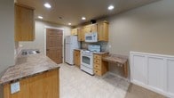 This two-story space is designed with a consistent, neutral aesthetic throughout, combining warm beige tones, light wood accents, and practical finishes. The bedrooms are carpeted and generously proportioned, with vaulted ceilings on the upper level adding a sense of openness. Several bedrooms feature double sliding or hinged wood panel closet doors, and windows fitted with blinds allow natural light to filter in. One lower-level room offers recessed ceiling lighting and a large window opening, making it a versatile space suited for a variety of uses.

The kitchen is equipped with light oak cabinetry, granite-style laminate countertops, white appliances including a range, microwave, and refrigerator, and recessed lighting overhead. A built-in desk area with matching countertop provides a convenient workspace. Tile flooring runs through the kitchen and bathrooms, offering durability and easy maintenance.

Both bathrooms follow a cohesive design, featuring light oak vanities with granite-style countertops, single sinks, tile flooring, and tub-shower combinations. One bathroom includes a dedicated dressing or vanity area with additional storage. Six-panel wood doors are used consistently throughout, contributing to a unified and polished interior character.