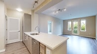 Located at 5648 Bay St in Emeryville, California, this well-appointed 2-bedroom, 2-bathroom residence offers a thoughtfully designed single-level layout. The open-concept kitchen and living area serves as the heart of the home, featuring a large central island with a white quartz countertop, an undermount sink, and modern cabinetry in a warm wood finish. The kitchen is equipped with stainless steel appliances, including a range, microwave, and refrigerator, complemented by a tiled backsplash. Track lighting and a skylight enhance the brightness of the space. The living area features wood-style flooring and a glass-paneled door that opens to a private balcony with greenery views, flooding the room with natural light. Both bedrooms are carpeted and generously proportioned, with the primary bedroom offering walk-in closet storage. The two bathrooms include wood-style vinyl flooring, and at least one features a full soaking tub. A dedicated closet with wire shelving provides additional storage. In-unit laundry hookups are also present. Neutral tones throughout the space create a clean, cohesive aesthetic that is both modern and inviting.