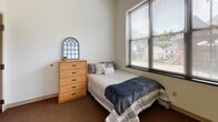 Located at 118 Prospect St in Ithaca, New York, this single-floor unit offers a practical and well-organized layout suited for everyday living. The kitchenette is efficiently designed with light wood cabinetry, granite-style countertops, a stainless steel sink, an electric range, a dishwasher, and an overhead microwave — providing all the essentials within a compact footprint. Light wood-style flooring runs through the kitchen area, contributing to a clean, bright aesthetic. The bedroom is a comfortably sized retreat featuring plush carpet flooring, tall ceilings, and large windows dressed with horizontal blinds that invite abundant natural light and offer views of the surrounding Ithaca neighborhood. The room accommodates a bed and a wooden desk with drawers, making it functional as both a sleeping and study space. A second bedroom area similarly features carpet flooring, a large window with neighborhood views, and ample wall space. The bathroom is accessed through a dark-toned wood door and features hardwood-style flooring, a bathtub with shower, and a clean, neutral palette. Throughout the unit, the design emphasizes practicality with light-toned walls and durable finishes, creating a cohesive and livable environment well-suited to the Ithaca setting.