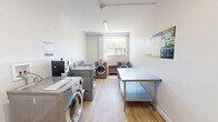 Located at 318–352 Patricia Ave in Kitchener, Ontario, this shared laundry facility offers a clean, well-organized space designed for practical, everyday use. The room is finished with light wood laminate flooring and bright white walls, creating a tidy and welcoming environment. Overhead fluorescent lighting ensures the space is well-lit throughout, supplemented by a window that brings in natural light and offers a view of the surrounding greenery.

The laundry room is equipped with multiple front-loading washing machines and dryers finished in a sleek silver tone, arranged efficiently along the walls to maximize usable floor space. A stainless steel folding and sorting table runs along one side of the room, providing ample surface area for handling laundry with ease. A utility sink is also present, adding further functionality to the space.

A digital payment terminal is conveniently mounted near the machines, offering a modern, card-free payment solution for users. Instructional and informational signage is posted on the walls, ensuring straightforward operation. The room is accessed through a solid entry door with secure hardware. The overall layout is thoughtfully arranged to accommodate multiple users comfortably, making this laundry room a highly functional shared amenity within the building.