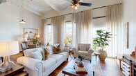Located at 1450 Greene St in Augusta, Georgia, this single-floor loft-style unit showcases a compelling blend of industrial heritage and refined contemporary design. Rich hardwood floors run throughout, anchoring each space with warmth and continuity, while soaring ceilings with exposed ductwork and white-painted wood beam detailing reflect the building's historic character.

The open-concept living area is a standout, featuring a wall of tall windows dressed with sheer linen curtains that invite generous natural light and offer views of the surrounding neighborhood. A ceiling fan overhead and ample seating create a comfortable, airy atmosphere. The kitchen is well-appointed with stainless steel appliances, white cabinetry extending to the ceiling, a classic subway tile backsplash, and dark countertops. An integrated dishwasher and open shelving add both function and style.

The bedrooms are calm and well-proportioned, with high ceilings, closet storage, and original structural columns that serve as subtle nods to the building's past. The bathroom includes a tub and shower combination. A dedicated entry area transitions smoothly into the main living spaces, reinforcing the unit's thoughtful, flowing layout throughout.