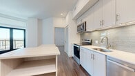 Located at 800 N 2nd St in Phoenix, AZ, this two-bedroom, two-bathroom residence offers a thoughtfully designed single-floor layout with a clean, contemporary aesthetic. The kitchen is a standout feature, showcasing white flat-front cabinetry extending to the ceiling, a light mosaic tile backsplash, white quartz countertops, and a full suite of stainless steel appliances including an electric range, over-the-range microwave, dishwasher, and refrigerator. A peninsula with open shelving provides additional prep and storage space. Rich wood-style flooring flows throughout the unit, adding warmth and continuity to the bright, white interior. Both bedrooms feature the same wood-style flooring and crisp white walls. The primary bedroom benefits from natural light through a window with blinds, while a secondary bedroom includes built-in corner shelving — a practical and stylish storage solution. The two bathrooms are finished with white cabinetry, quartz vanity tops, and glass-enclosed walk-in showers with large-format tile surrounds. A dedicated closet adds further storage. A smart thermostat is also featured, contributing to the modern, functional character of this well-appointed Phoenix residence.