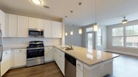 Located in Atlanta, GA (30318), this single-floor residence offers a thoughtfully designed open-concept layout with contemporary finishes throughout. The kitchen is a standout feature, showcasing white shaker cabinetry, granite countertops, a classic white subway tile backsplash, and a full suite of stainless steel appliances including a gas range, built-in microwave, dishwasher, and refrigerator. A central island with a stainless steel sink and pendant lighting above creates an ideal space for both meal preparation and casual dining. A built-in wine rack adds a refined touch to the living area transition. The expansive living room benefits from an abundance of natural light through multiple large windows and a glass door leading to a private balcony, complemented by rich dark hardwood-style flooring and a ceiling fan overhead. Bedrooms are carpeted for comfort and receive ample natural light. The bathrooms are finished with granite-topped white vanities and hardwood-style flooring; one bathroom features a soaking tub, while another offers a glass-enclosed walk-in shower. Neutral wall tones and clean architectural lines create a cohesive, modern ambiance throughout the entire space.