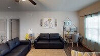 This single-floor residence offers a thoughtfully designed open-concept layout that seamlessly connects the living, dining, and kitchen areas. The living room features wood-look flooring, a ceiling fan, and comfortable seating, creating a welcoming and functional gathering space. A dedicated media area with a wall-mounted television and ladder shelving adds versatility to the layout.

The kitchen is a standout feature, showcasing warm honey-toned cabinetry, granite-style countertops, and a full suite of stainless steel appliances, including a refrigerator, microwave, and range. A peninsula with bar seating provides both additional prep space and casual dining options, while an adjacent dining nook offers a more formal setting.

The residence includes multiple bedrooms, each finished with plush carpet, ceiling fans, and windows that allow natural light to filter in. The bedrooms offer a calm, comfortable atmosphere well-suited for rest and relaxation.

Two bathrooms serve the residence, each equipped with a tub-shower combination, granite-style vanity countertops, and rich wood-toned cabinetry. The bathrooms maintain a clean, functional aesthetic consistent with the rest of the home.

Throughout the space, neutral wall tones, consistent flooring choices, and arched interior doors contribute to a cohesive and inviting overall ambiance.