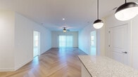This single-floor unit showcases a thoughtfully designed open layout with a consistent, contemporary aesthetic throughout. The living and dining areas are anchored by striking herringbone-patterned hardwood flooring that extends through the main spaces, complemented by crisp white walls and recessed lighting. A ceiling fan with a light fixture overhead and vertical blinds covering a sliding glass door allow for both airflow and natural light control, creating a bright, airy ambiance.

The kitchen is well-appointed with rich dark cabinetry, granite countertops, a mosaic tile backsplash, and a full suite of stainless steel appliances including a refrigerator, range, microwave, and dishwasher. A central island with a granite surface provides additional workspace, illuminated by two globe pendant lights overhead.

The bedrooms feature plush wall-to-wall carpeting, ceiling fans, and large windows offering outdoor views, filling each room with natural light. The bathroom is finished with decorative patterned floor tile, a granite-topped dark vanity, an undermount sink with matte black fixtures, and a shower-tub combination. Clean lines and neutral tones throughout create a cohesive, modern living environment.