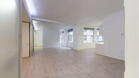 Located at 600–666 Vincent Ave in Cleveland, Ohio, this single-floor unit presents a clean, modern aesthetic defined by an all-white palette, light wood-style flooring, and an open, airy layout. The main living area is generously proportioned, benefiting from multiple windows that invite natural light and offer views of the surrounding urban streetscape. Crisp white walls and smooth ceilings with subtle beam detailing contribute to a bright, uncluttered atmosphere throughout.

The galley-style kitchen runs along one wall and features white cabinetry extending to the ceiling, white appliances including a range, built-in microwave, and refrigerator, along with light countertops and under-cabinet lighting. A window above the counter brings in additional daylight, enhancing the kitchen's functional, streamlined character.

A distinctive feature of the space is its use of glass-panel sliding partitions, which define separate areas while preserving the open feel of the interior. These frosted and clear glass dividers are framed in sleek aluminum and include recessed linear lighting overhead, lending a contemporary, flexible quality to the layout.

The bathroom is finished in an equally clean style, with small white mosaic floor tile, a full soaking tub with tiled surround, a wall-mounted sink, and a mirrored medicine cabinet. Every element of this space reflects a cohesive, minimalist design sensibility.
