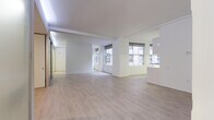 Located at 600–666 Vincent Ave in Cleveland, Ohio, this single-floor unit presents a clean, modern aesthetic defined by an all-white palette, light wood-style flooring, and an open, airy layout. The main living area is generously proportioned, benefiting from multiple windows that invite natural light and offer views of the surrounding urban streetscape. Crisp white walls and smooth ceilings with subtle beam detailing contribute to a bright, uncluttered atmosphere throughout.

The galley-style kitchen runs along one wall and features white cabinetry extending to the ceiling, white appliances including a range, built-in microwave, and refrigerator, along with light countertops and under-cabinet lighting. A window above the counter brings in additional daylight, enhancing the kitchen's functional, streamlined character.

A distinctive feature of the space is its use of glass-panel sliding partitions, which define separate areas while preserving the open feel of the interior. These frosted and clear glass dividers are framed in sleek aluminum and include recessed linear lighting overhead, lending a contemporary, flexible quality to the layout.

The bathroom is finished in an equally clean style, with small white mosaic floor tile, a full soaking tub with tiled surround, a wall-mounted sink, and a mirrored medicine cabinet. Every element of this space reflects a cohesive, minimalist design sensibility.