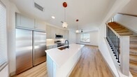 Located at 9590 E Northfield Blvd in Denver, CO, this two-story home offers a thoughtfully designed layout spread evenly across two floors. The main level features an open-concept kitchen and living area finished with light hardwood flooring and crisp white walls that create a bright, airy atmosphere. The kitchen is a standout space, showcasing a large central island with a white quartz countertop, stainless steel appliances including a full-size refrigerator, microwave, and range, and soft gray shaker-style cabinetry. Stylish pendant lights hang above the island, complementing the ceiling fan that anchors the adjacent living area. Natural light flows in through large windows. A clean staircase with wood treads and a streamlined handrail connects the two floors. The upper level hosts three bedrooms, each featuring plush carpeting, ceiling fans, and natural light from multiple windows. Each bedroom includes its own closet with built-in shelving and hanging rods. Three well-appointed bathrooms feature tile flooring and clean, modern fixtures. A dedicated laundry room with full-size Samsung washer and dryer adds everyday convenience. The home's consistent use of neutral tones and modern finishes gives it a cohesive, contemporary feel throughout.