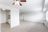 This single-floor residence offers a practical and comfortable layout spread across several well-defined living spaces. The main living area is generously proportioned, finished with neutral wall-to-wall carpeting and topped with a ceiling fan with integrated lighting. The open feel of the room is complemented by its connection to a secondary carpeted space that leads to the unit's entry door.

The kitchen is efficiently designed with light gray cabinetry extending to the ceiling for ample storage, laminate countertops, tile flooring, and a full suite of white appliances including a gas range, dishwasher, and refrigerator. A sink with overhead cabinet access rounds out the functional workspace.

The bedrooms are comfortably sized, each featuring plush carpeting, natural light through horizontal-blind-fitted windows that offer outdoor views, and generous closet space. One bedroom includes a direct connection to the bathroom.

The bathroom presents a retro aesthetic with pink ceramic tile wainscoting, a tub-shower combination with a coordinating tile surround featuring a checkerboard accent pattern, a wall-mounted vanity mirror, and a white sink set into a wood-toned cabinet base.