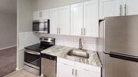 Located at 213 S Macdade Blvd in Glenolden, PA, this single-floor unit offers a thoughtfully updated interior with a clean, neutral aesthetic throughout. The kitchen serves as a standout feature, showcasing white shaker-style cabinetry with brushed nickel hardware, variegated granite countertops, and a classic white subway tile backsplash. A full suite of stainless steel appliances — including an electric range, over-the-range microwave, dishwasher, and refrigerator — completes the space. Light wood-look flooring runs through the kitchen, lending a warm, modern contrast to the crisp white cabinetry.

The living and sleeping areas are finished with wall-to-wall carpet in a neutral tone, contributing to a quiet and comfortable atmosphere. Windows in each room allow natural light to filter in, and baseboard heating along with wall-mounted air conditioning units provide year-round climate control. The rooms are finished in soft gray tones with clean white trim throughout.

The bathroom features a white vanity, light gray tile flooring, and a panel-style door, maintaining the unit's consistent, updated aesthetic. The overall layout, as seen in the floor plan, is efficiently arranged, making practical use of the available space.