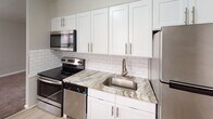 Located at 213 S Macdade Blvd in Glenolden, PA, this single-floor unit offers a thoughtfully updated interior with a clean, neutral aesthetic throughout. The kitchen serves as a standout feature, showcasing white shaker-style cabinetry with brushed nickel hardware, variegated granite countertops, and a classic white subway tile backsplash. A full suite of stainless steel appliances — including an electric range, over-the-range microwave, dishwasher, and refrigerator — completes the space. Light wood-look flooring runs through the kitchen, lending a warm, modern contrast to the crisp white cabinetry.

The living and sleeping areas are finished with wall-to-wall carpet in a neutral tone, contributing to a quiet and comfortable atmosphere. Windows in each room allow natural light to filter in, and baseboard heating along with wall-mounted air conditioning units provide year-round climate control. The rooms are finished in soft gray tones with clean white trim throughout.

The bathroom features a white vanity, light gray tile flooring, and a panel-style door, maintaining the unit's consistent, updated aesthetic. The overall layout, as seen in the floor plan, is efficiently arranged, making practical use of the available space.