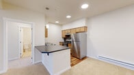 This single-floor residence at 4250 E Poleline Ave in Post Falls, Idaho, offers a thoughtfully designed layout with a clean, neutral aesthetic throughout. The open-concept kitchen serves as a central feature, equipped with stainless steel appliances including a full-size refrigerator and electric range, warm-toned wood cabinetry, and dark countertops. A white peninsula with a built-in sink provides additional workspace and casual seating, seamlessly connecting the kitchen to the adjacent living area. Recessed lighting and a pendant light above the peninsula keep the space bright and functional.

The living area features plush carpet underfoot and transitions to hardwood-style flooring in the kitchen zone, offering a pleasant contrast in materials. A full-light entry door flanked by windows invites natural light into the living space, which also benefits from baseboard heating along the perimeter walls. The bedrooms are carpeted and generously sized, with at least one room featuring a window with exterior views of the surrounding community. The bathroom is finished with a wood-tone vanity, white countertop, full tub-shower combination, and hardwood-style flooring, maintaining a consistent, clean design throughout the unit.