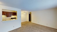 This single-floor unit offers two bedrooms and one bathroom within a well-organized layout designed for efficient use of space. The living area is carpeted throughout, providing a warm and comfortable feel underfoot, and is illuminated by a classic chandelier that adds a touch of elegance to the room. The textured ceiling adds visual depth to the space.

A pass-through window connects the kitchen to the living area, creating an open sightline between the two spaces while maintaining a defined separation. The kitchen is equipped with dark cabinetry and an electric range, offering a functional cooking environment. The neutral, cream-toned walls throughout the unit create a clean and versatile backdrop suited to a variety of décor styles.

A hallway visible from the living area leads to the remaining rooms, including the bedrooms and bathroom, maintaining a practical flow throughout the unit. The overall ambiance is straightforward and functional, with understated finishes that provide a comfortable, move-in-ready living environment suitable for a range of occupants.