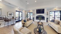 This single-floor community clubhouse in Greensboro, NC (27409) offers a thoughtfully designed layout with a wide range of amenities. The grand entrance foyer sets an impressive tone, featuring soaring double-height ceilings, light hardwood flooring, and a dramatic round accent table topped with a striking monstera plant arrangement. French doors with frosted glass panels open into the main interior, where the open-plan layout connects multiple functional zones seamlessly.

The lounge area is a welcoming gathering space anchored by a wall-mounted flat-screen television above a sleek fireplace with a dark tile surround. Large glass doors fill the room with natural light and provide views of the surrounding community. Adjacent to the lounge, a fully equipped kitchen features white cabinetry, a subway tile backsplash, stainless steel appliances, dark granite countertops, and a central island with bar seating — ideal for catering or communal use.

The game room accommodates a full-size billiards table and opens to an outdoor seating area and glass-walled business center. The business center includes a built-in granite-topped workstation with multiple workstations, ergonomic seating, and printing equipment. A cozy café nook with wicker bar stools and large windows rounds out the space. A fitness center with cardio equipment is also accessible from the main corridor.