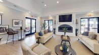 This single-floor community clubhouse in Greensboro, NC (27409) offers a thoughtfully designed layout with a wide range of amenities. The grand entrance foyer sets an impressive tone, featuring soaring double-height ceilings, light hardwood flooring, and a dramatic round accent table topped with a striking monstera plant arrangement. French doors with frosted glass panels open into the main interior, where the open-plan layout connects multiple functional zones seamlessly.

The lounge area is a welcoming gathering space anchored by a wall-mounted flat-screen television above a sleek fireplace with a dark tile surround. Large glass doors fill the room with natural light and provide views of the surrounding community. Adjacent to the lounge, a fully equipped kitchen features white cabinetry, a subway tile backsplash, stainless steel appliances, dark granite countertops, and a central island with bar seating — ideal for catering or communal use.

The game room accommodates a full-size billiards table and opens to an outdoor seating area and glass-walled business center. The business center includes a built-in granite-topped workstation with multiple workstations, ergonomic seating, and printing equipment. A cozy café nook with wicker bar stools and large windows rounds out the space. A fitness center with cardio equipment is also accessible from the main corridor.