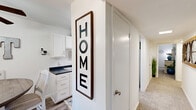 Located at 4981 Hunt Club Rd in Winston-Salem, NC, this single-story 2-bedroom, 1-bathroom home offers a well-organized and inviting layout. The living room is bright and welcoming, featuring plush carpeting, natural light from curtained windows, and a large decorative mirror that enhances the sense of space. It flows seamlessly into the combined dining and kitchen area, where white cabinetry and dark countertops create a clean, functional workspace. A hallway connects the main living areas to the bedrooms and bathroom, lined with an impressive five closets that provide exceptional storage throughout the home. The spacious primary bedroom features carpeted floors, natural light from a window with lush outdoor views, and ample room for full bedroom furnishings. The second bedroom is equally comfortable, with carpet flooring and its own natural light. The full bathroom is finished with wood-look flooring, a tub-shower combination, a white vanity, and clean, bright finishes. A dedicated in-unit laundry area adds everyday convenience. Throughout the home, neutral walls and consistent flooring choices create a cohesive, move-in-ready feel that is both practical and warm.